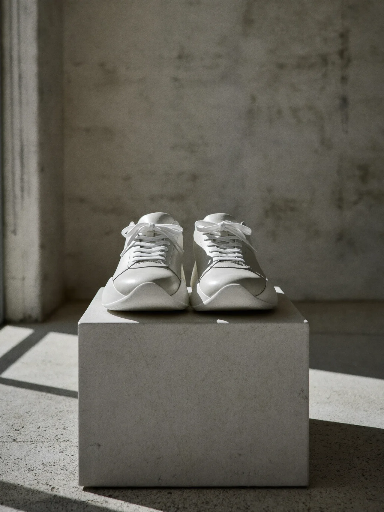 Weißer Leder-Low-Top-Sneaker auf hellem Betonsockel im weichen Seitenlicht